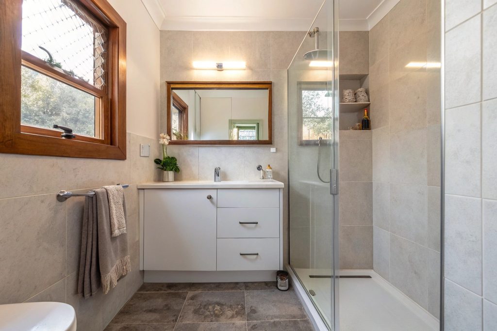 Small ensuite bathroom with wall-mounted vanity and frameless corner shower in a Hobart home